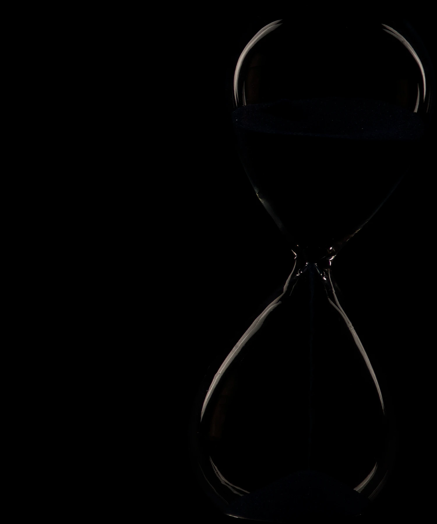 Minimalist glass hourglass illuminated against a dark background.
