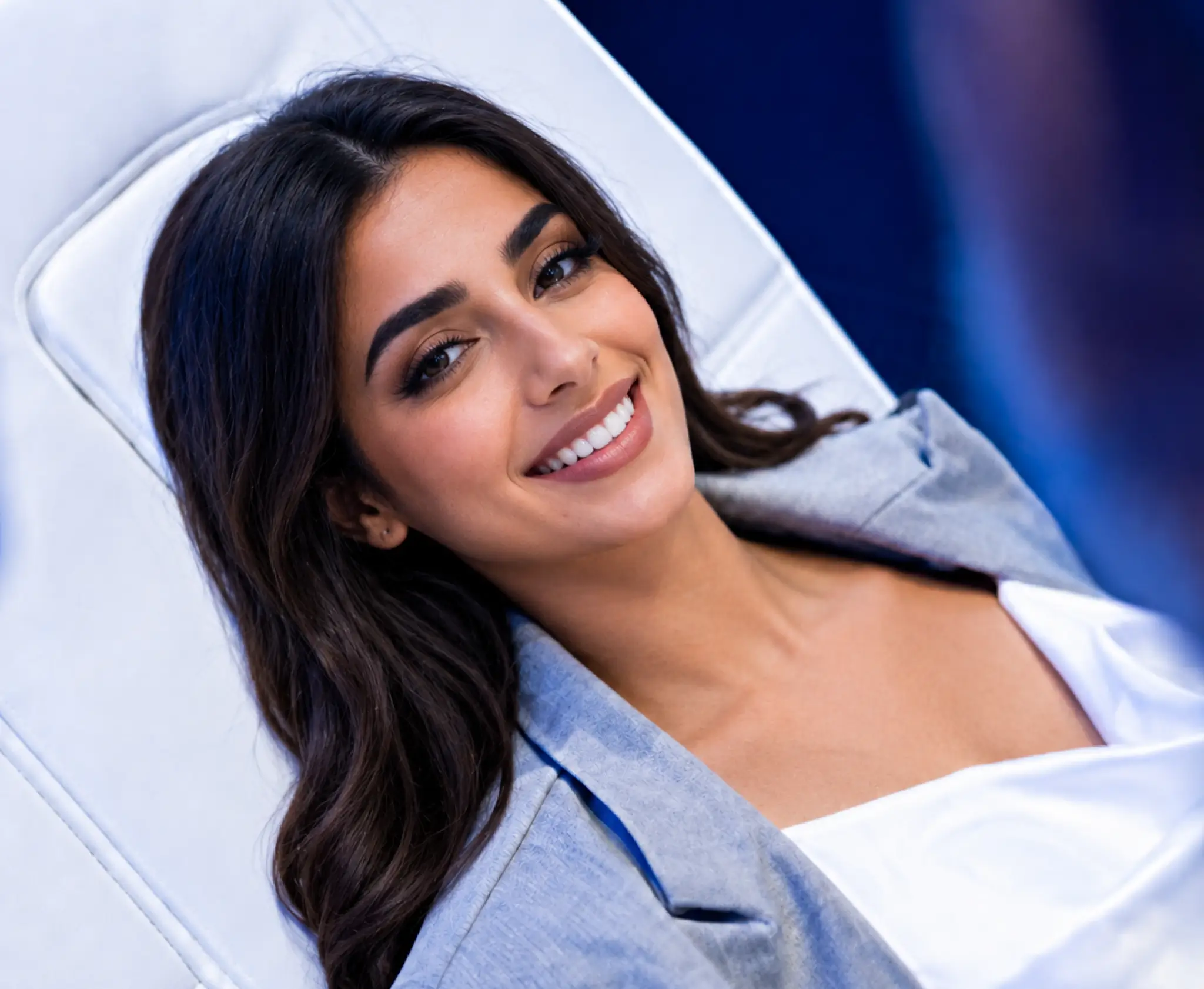 A smiling woman with dark hair reclining comfortably in a white treatment chair
