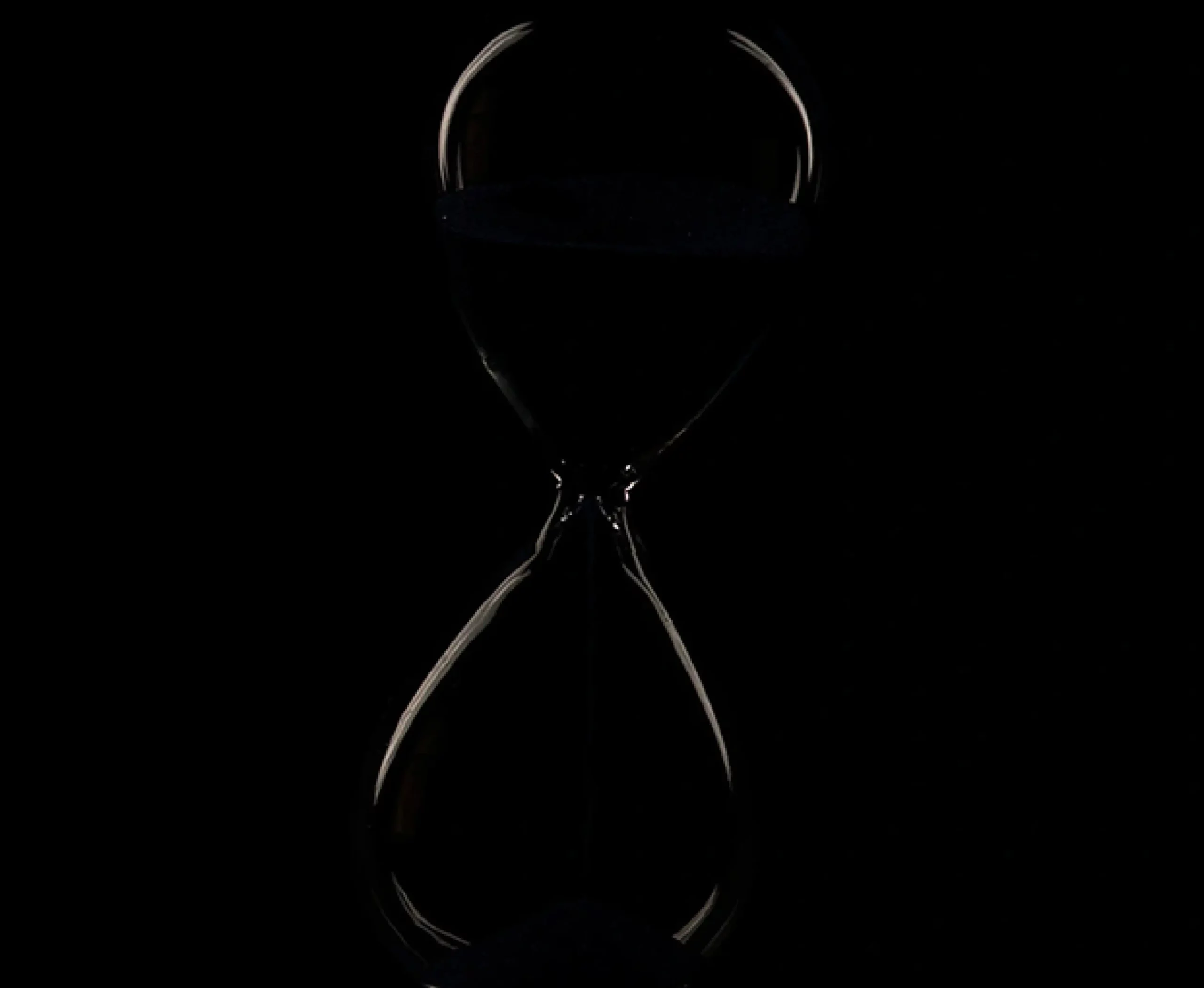 A minimalist, low-key photograph of a glass hourglass set against a dark background, with sleek light highlights outlining its silhouette.