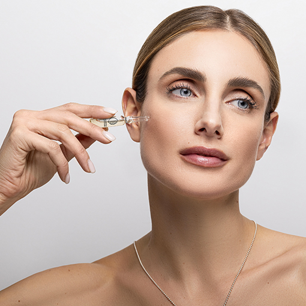 A woman holding a skincare glass ampoule near her face.